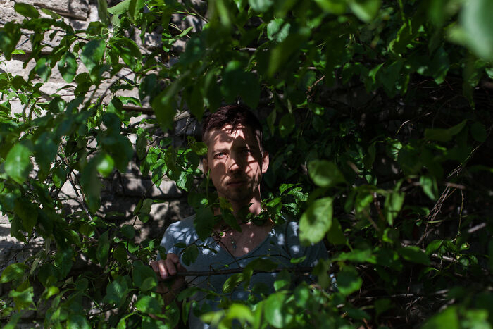 Man hidden among dense green leaves, symbolizing local dangers that are a normal part of life for some people.