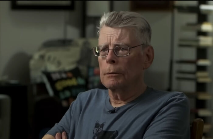 Older man with glasses and gray hair speaking about local dangers in a casual indoor setting with bookshelves in background