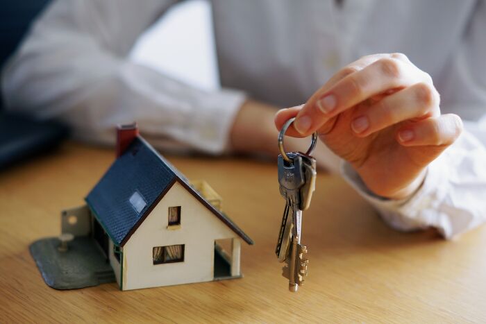 Person holding house keys next to a miniature house, illustrating local dangers that are part of everyday life.