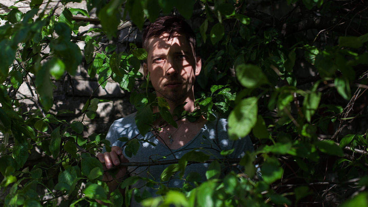 Man standing hidden among dense green leaves, illustrating local dangers that are a normal part of life.
