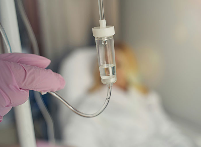 Hospital IV drip held by gloved hand with blurred patient in background, highlighting man trapped in hospital story. Hospital IV drip held by gloved hand with blurred patient in background, highlighting man trapped in hospital story.