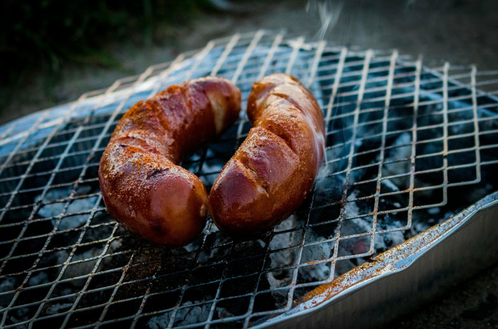 Two grilled hot dogs on a wire grill emitting smoke, highlighting concerns about human DNA in hot dogs.