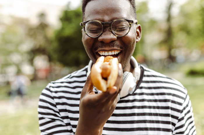 Man wearing glasses and striped shirt about to eat hot dog, highlighting human DNA in hot dogs concern.
