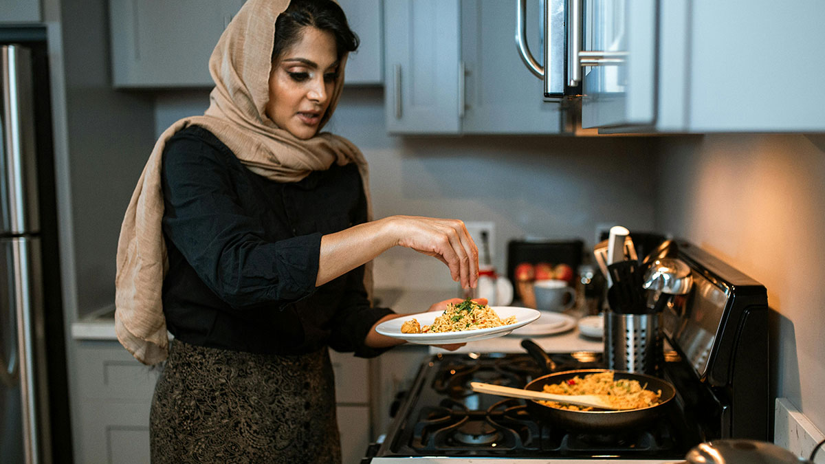 Woman wearing a headscarf cooking traditional food in kitchen, representing wife adopting husbandu2019s culture and family life.