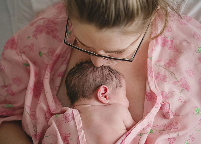 Mother in pink floral robe holding and bonding with newborn baby resting on her chest after cesarean birth. Mother in pink floral robe holding and bonding with newborn baby resting on her chest after cesarean birth.