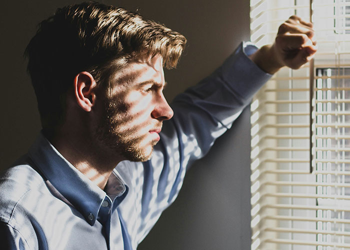 Man in a blue shirt looking out blinds with a serious expression, reflecting on bonding struggles with cesarean baby daughter. Man in a blue shirt looking out blinds with a serious expression, reflecting on bonding struggles with cesarean baby daughter.