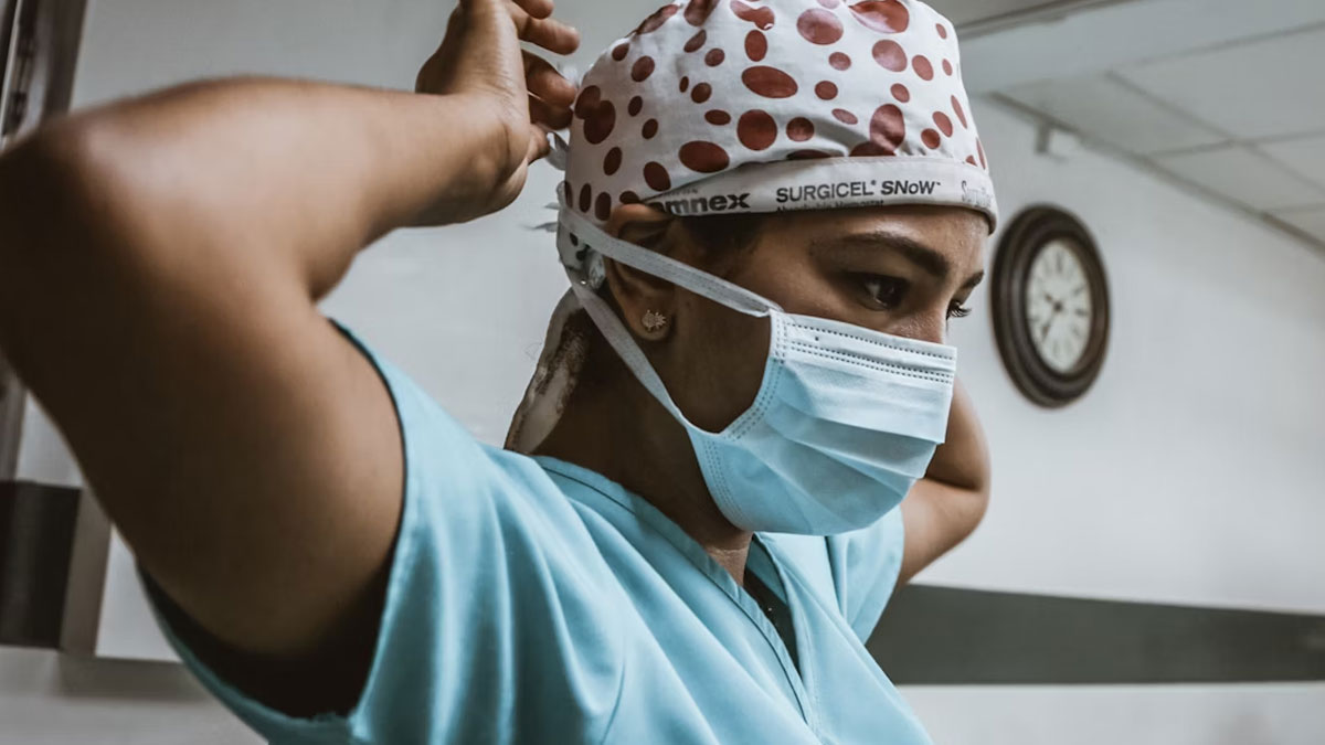 Medical professional in surgical scrubs and mask preparing for a medical case in a clinical setting.