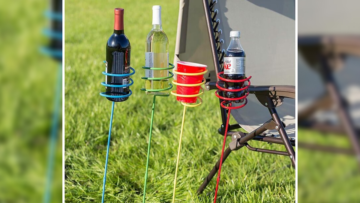 Colorful outdoor dining drink holders staked on grass next to a chair with bottles and cups for picnic essentials.
