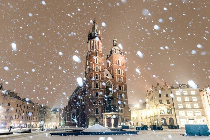 Snowfall at a historic European square with illuminated old buildings, illustrating European netizens correcting country facts.