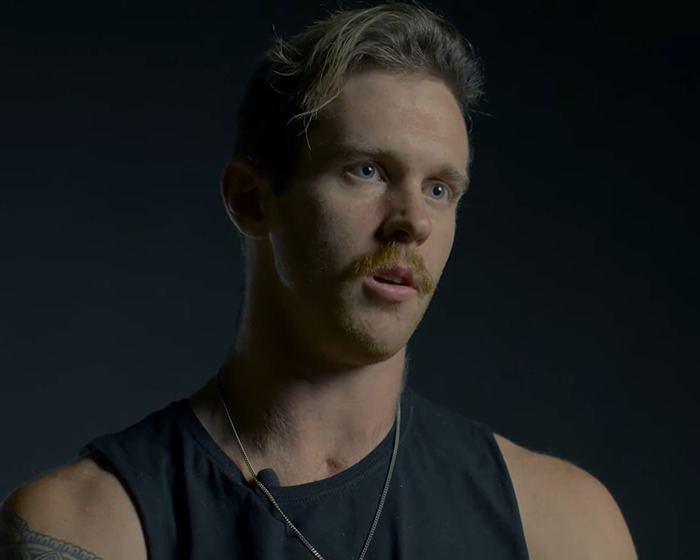 Young man with tattoo and mustache in dark tank top sharing experience as a beginner Jiu-Jitsu student after tragic freak accident Young man with tattoo and mustache in dark tank top sharing experience as a beginner Jiu-Jitsu student after tragic freak accident