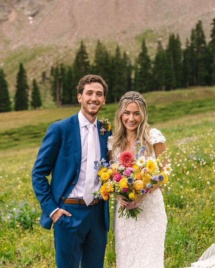 Newlyweds posing outdoors with a colorful bouquet amidst green fields and trees on their honeymoon. Newlyweds posing outdoors with a colorful bouquet amidst green fields and trees on their honeymoon.