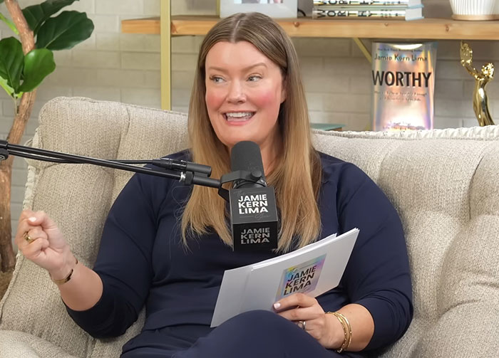Woman hosting a podcast discussing Meghan Markle's insufferable interview with a microphone and notes in a casual studio setting. Woman hosting a podcast discussing Meghan Markle's insufferable interview with a microphone and notes in a casual studio setting.