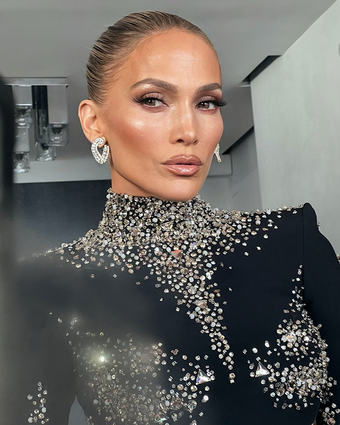 Jennifer Lopez posing in a black outfit adorned with sparkling crystals, facing camera with a neutral expression indoors. Jennifer Lopez posing in a black outfit adorned with sparkling crystals, facing camera with a neutral expression indoors.