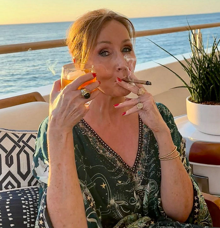 A woman smoking a cigar and holding a drink on a balcony overlooking the ocean, captured at sunset. A woman smoking a cigar and holding a drink on a balcony overlooking the ocean, captured at sunset.