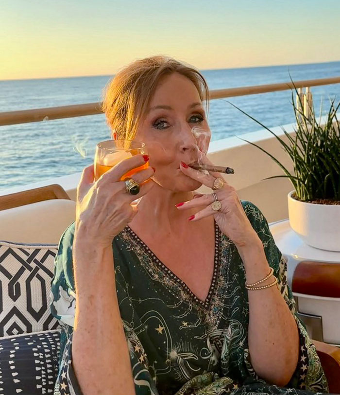 Woman smoking a cigar and holding a drink outdoors with ocean view, related to Pedro Pascal defending criticism of JK Rowling. Woman smoking a cigar and holding a drink outdoors with ocean view, related to Pedro Pascal defending criticism of JK Rowling.
