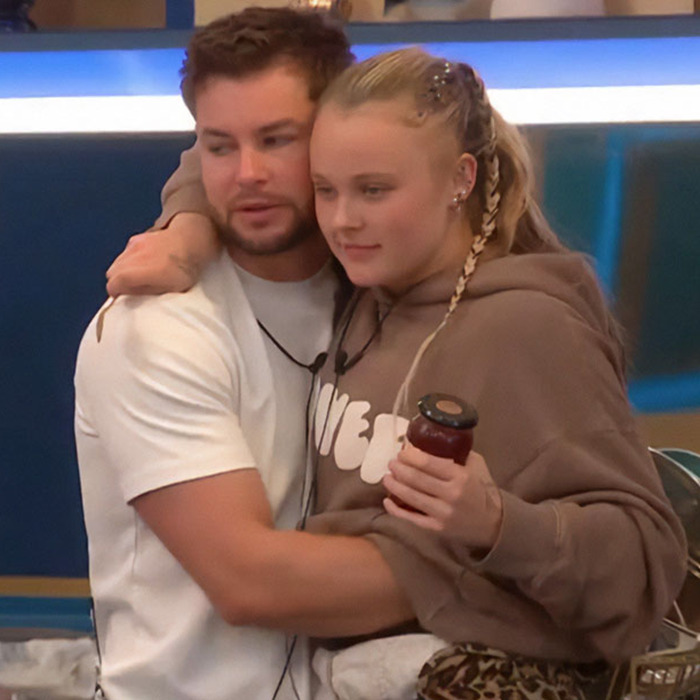 JoJo Siwa hugging a man indoors, wearing a brown hoodie, with a post about orientation sparking Pride Month backlash. JoJo Siwa hugging a man indoors, wearing a brown hoodie, with a post about orientation sparking Pride Month backlash.