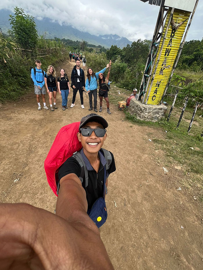 Group of hikers posing on a dirt trail near an Indonesian volcano during a tourist hike with guide and backpacks.