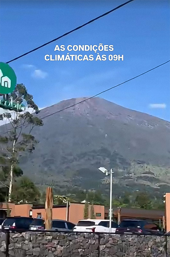 Indonesian volcano with clear sky above, showing parking area and text about weather conditions at 9 AM.