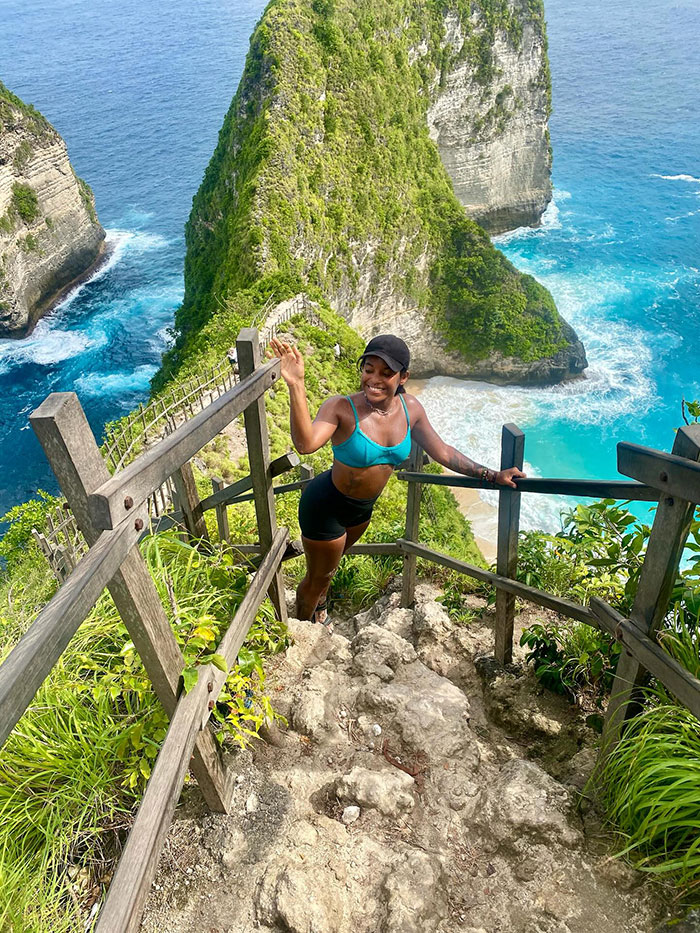 Female tourist hiking on steep trail near Indonesian volcano overlooking ocean and cliffs during outdoor adventure
