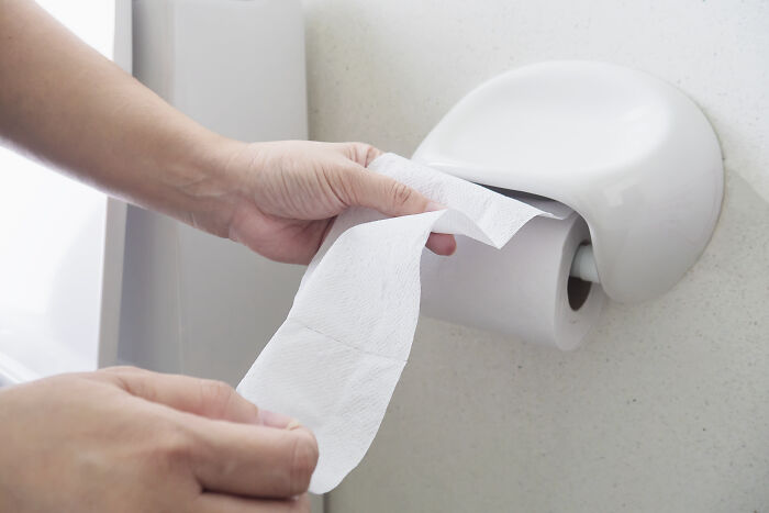 Person pulling toilet paper from a holder, symbolizing coworker diabolical things to report to HR issues.