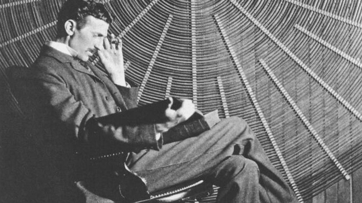 Nikola Tesla seated, reading a book, surrounded by coils, representing his influential legacy in electrical engineering.
