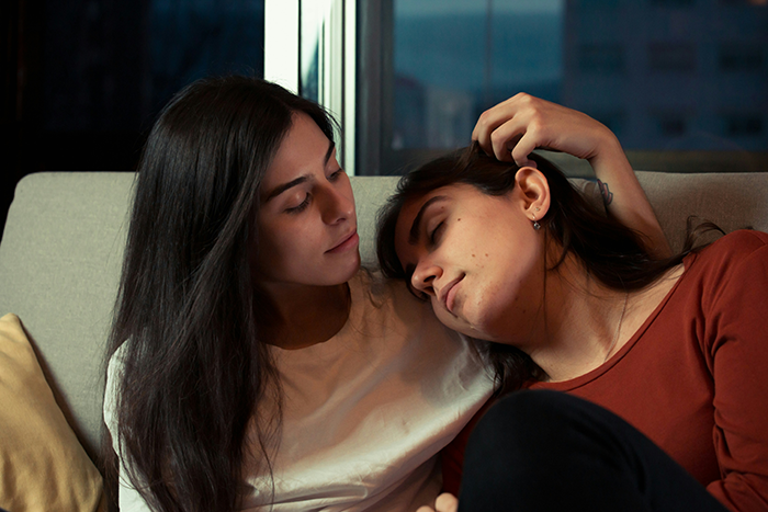 Two women sitting close together, one gently touching the other's hair, showing affection in a calm evening setting. Two women sitting close together, one gently touching the other's hair, showing affection in a calm evening setting.