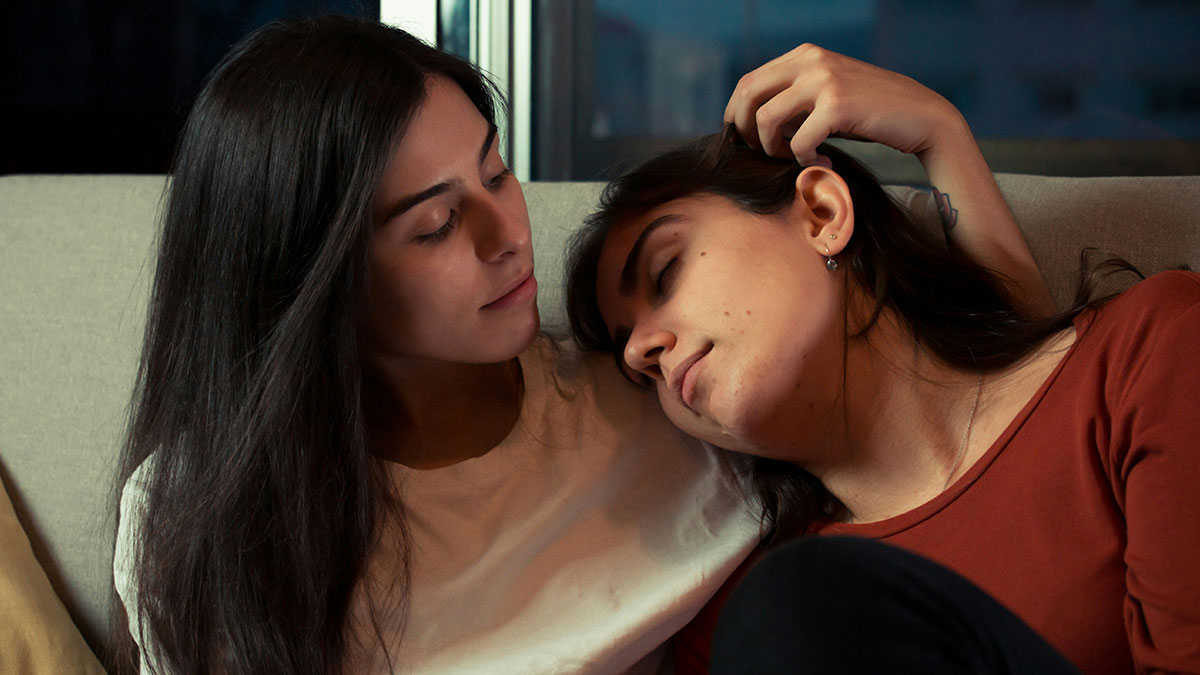 Woman dates someone 16 years older, tender moment between two women showing affection on a couch at home.