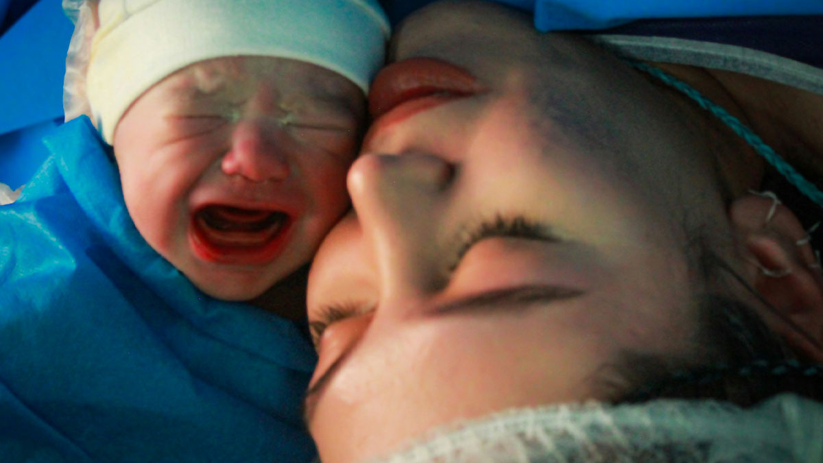 Newborn crying next to mother moments after childbirth, highlighting pregnancy and postpartum emotional bond.