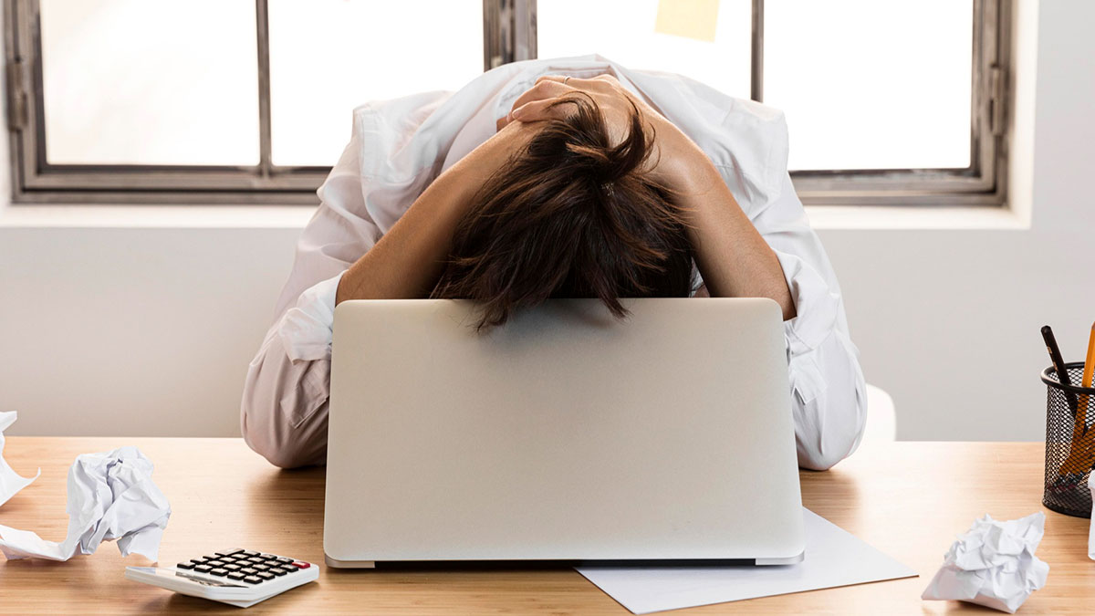 Person frustrated at laptop with crumpled papers and calculator, showing commitment to a lie way too hard concept.