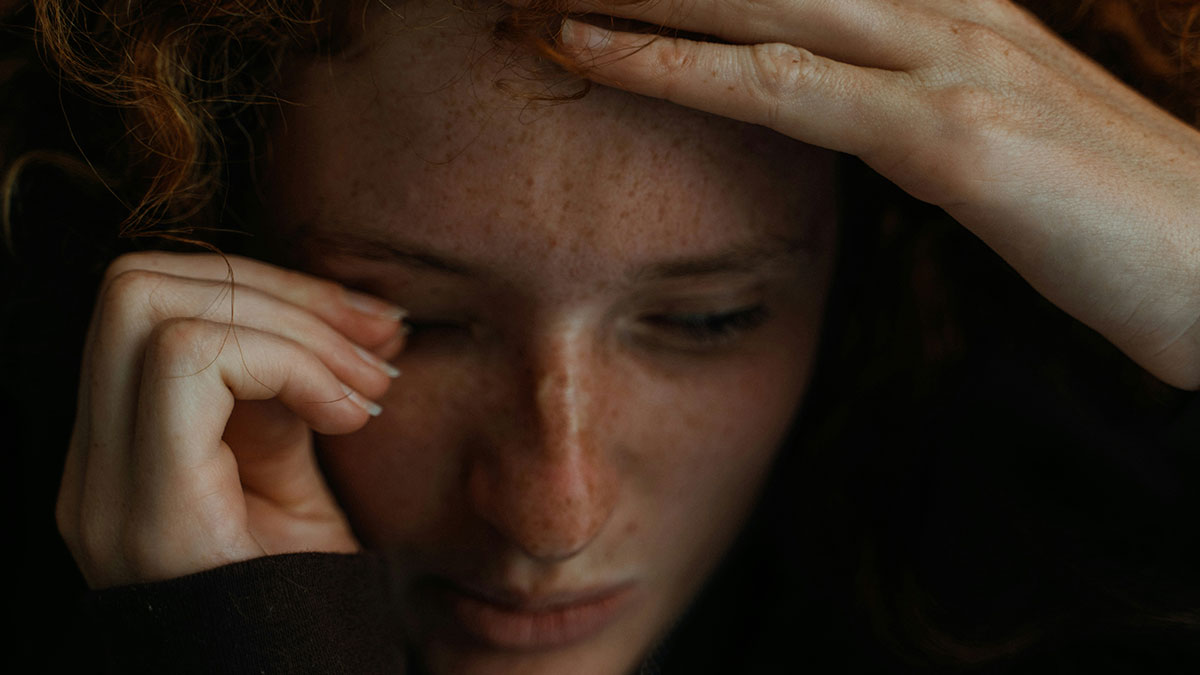 Close-up of a distressed woman with freckles touching her forehead, illustrating intense emotional moments in therapy sessions.