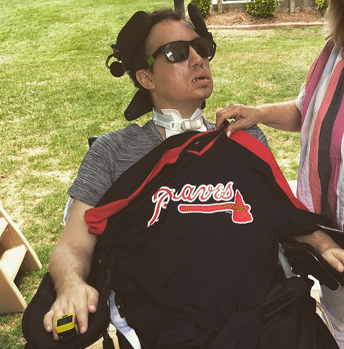 Man in a wheelchair with locked-in syndrome after chiropractor visit, wearing sunglasses and holding a remote control. Man in a wheelchair with locked-in syndrome after chiropractor visit, wearing sunglasses and holding a remote control.