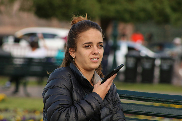 Young woman sitting on a bench outdoors, speaking into her smartphone, symbolizing longtime friends and ghost friend birthday calls. Young woman sitting on a bench outdoors, speaking into her smartphone, symbolizing longtime friends and ghost friend birthday calls.