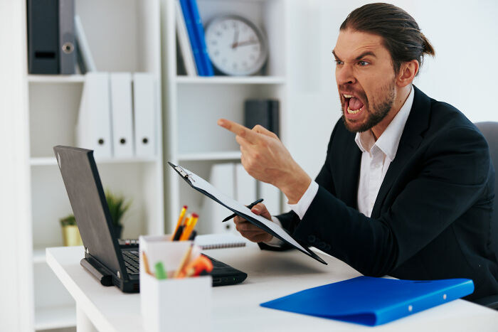 Angry man in business suit pointing finger and yelling at laptop, illustrating awful people in certain professions.