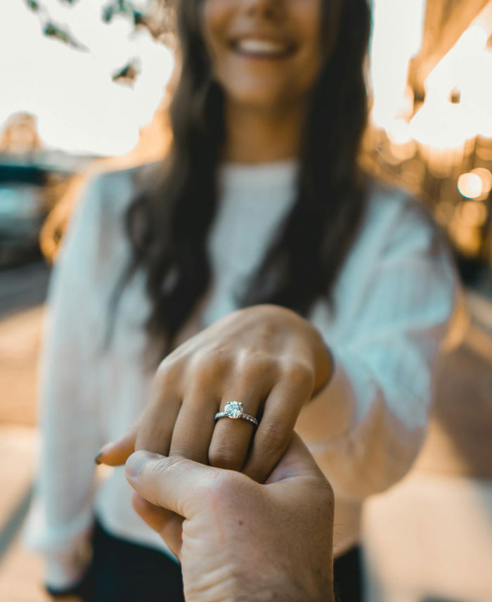 Woman refusing to wear engagement ring, holding fiancé's hand outdoors with a blurred background at sunset. Woman refusing to wear engagement ring, holding fiancé's hand outdoors with a blurred background at sunset.
