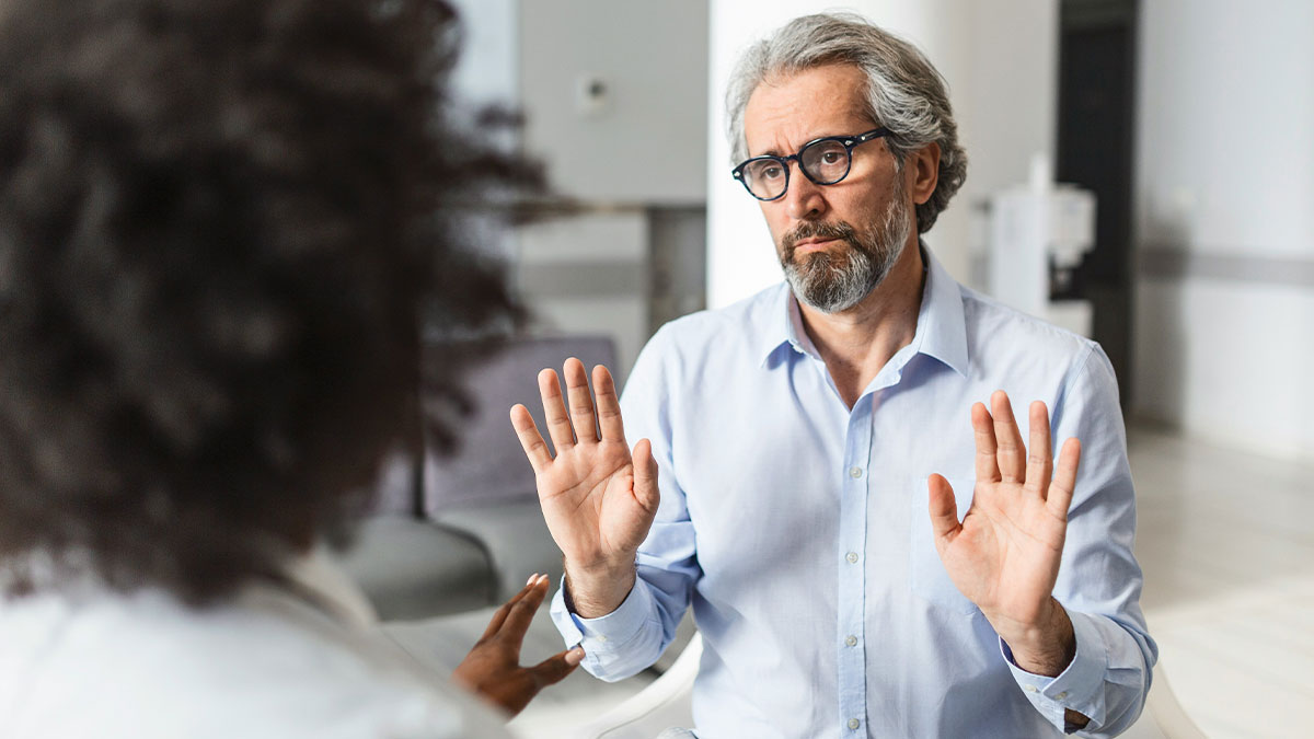Mature man with glasses raising hands while talking to a woman, representing men who stand out in romantic moments.