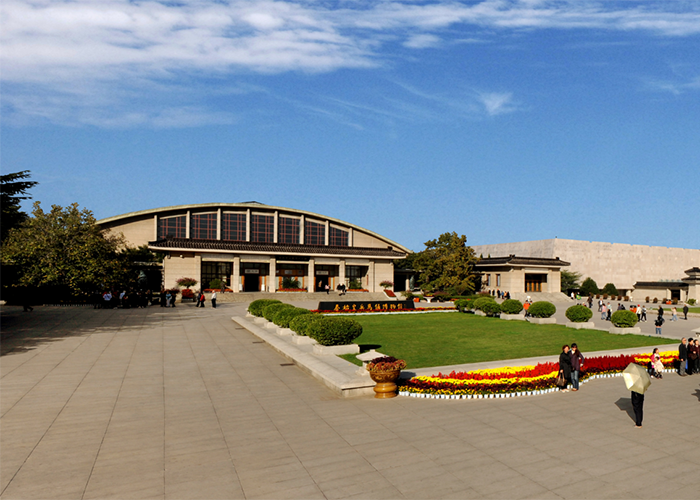 Tourists visiting an ancient historic site with 2000-year-old statues near a large open plaza and garden area.