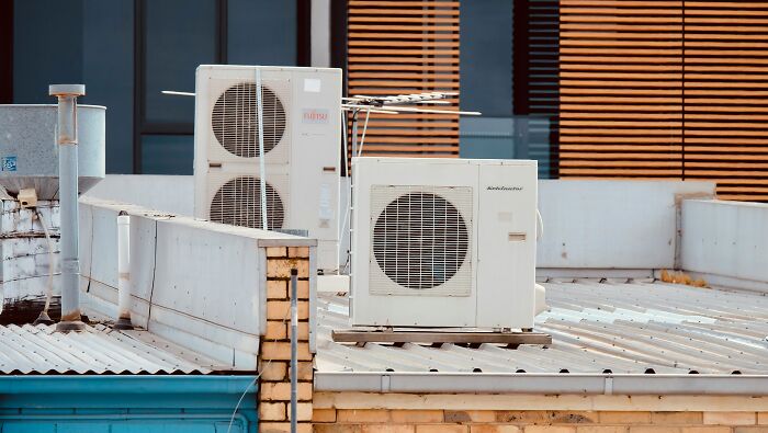 Air conditioning units on a rooftop with piping and a modern building facade in the background, highlighting historical facts.