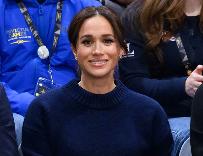 Meghan Markle smiling in a navy sweater at an event, related to Harry and Meghan's insufferable interview roast. Meghan Markle smiling in a navy sweater at an event, related to Harry and Meghan's insufferable interview roast.