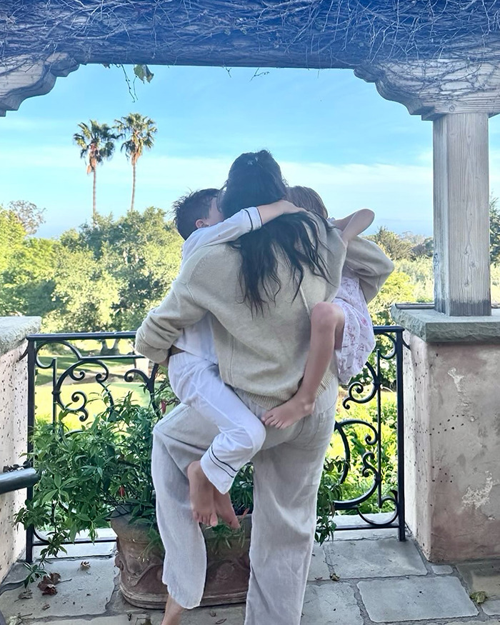 Meghan Markle carrying her kids outdoors on a sunny day with greenery and palm trees in the background. Meghan Markle carrying her kids outdoors on a sunny day with greenery and palm trees in the background.