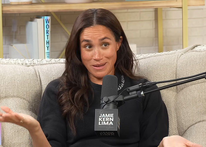 Meghan Markle speaking during an interview on the Jamie Kern Lima show with a playful expression on a beige couch. Meghan Markle speaking during an interview on the Jamie Kern Lima show with a playful expression on a beige couch.
