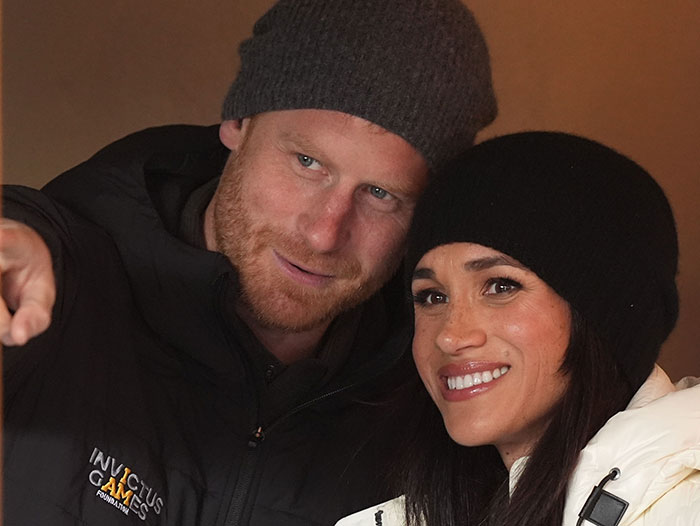 Prince Harry and Meghan Markle wearing winter hats and jackets, smiling and posing closely together. Prince Harry and Meghan Markle wearing winter hats and jackets, smiling and posing closely together.