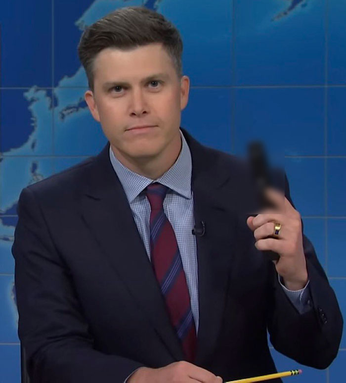 Man in a suit and tie holding a blurred object, appearing serious in a studio with a world map backdrop. Man in a suit and tie holding a blurred object, appearing serious in a studio with a world map backdrop.