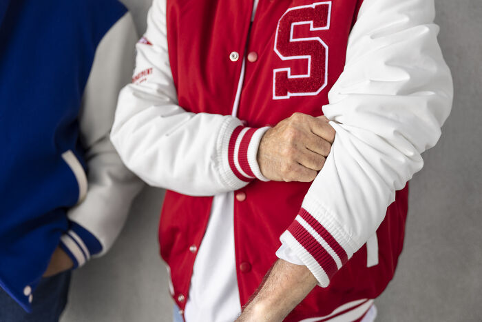 Two adults wearing high school varsity jackets, showing they never moved on from their glory days in school.