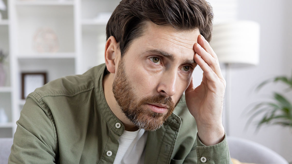 Man with beard and brown hair looks worried holding his forehead, illustrating concerns about forcing child to get tattoo