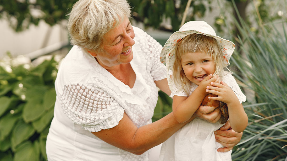 Grandmother and smiling 3-year-old granddaughter outdoors, enjoying time together before Hawaii vacation surprise.