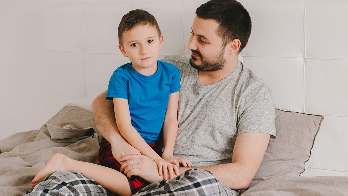 Man in pajamas comforting young boy on bed, illustrating absent grandma trying to reconnect after 25 years concept