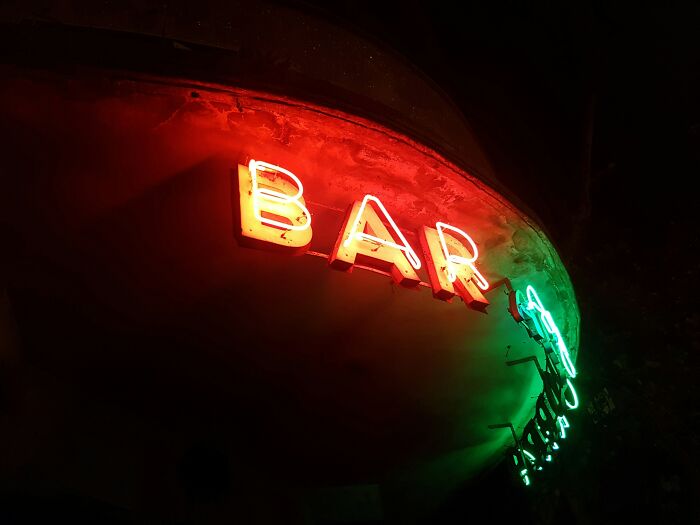Neon bar sign glowing red and green in a dark setting, illustrating stories of people ruining their entire life.