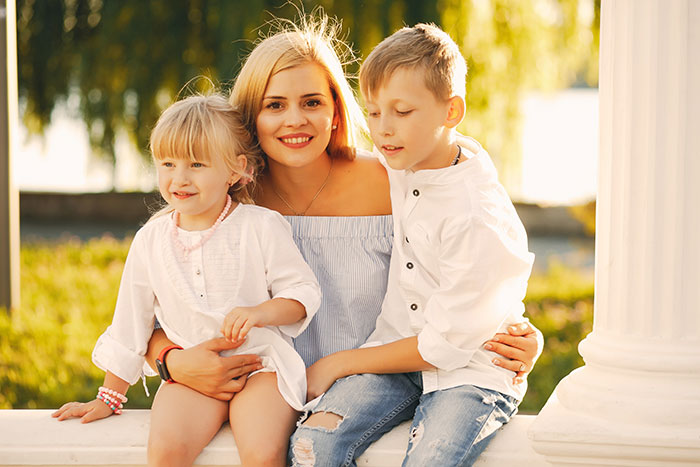 Woman sitting outdoors with two children, illustrating mom expects endless babysitting from sister instead of a trip. Woman sitting outdoors with two children, illustrating mom expects endless babysitting from sister instead of a trip.