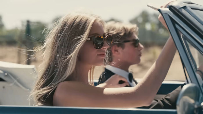 Young nepo grandbaby wearing sunglasses, driving a convertible with a passenger, in a sunny outdoor setting. Young nepo grandbaby wearing sunglasses, driving a convertible with a passenger, in a sunny outdoor setting.