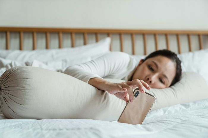 Woman struggling in life lying on bed holding phone, reflecting relationship challenges and emotional torment.
